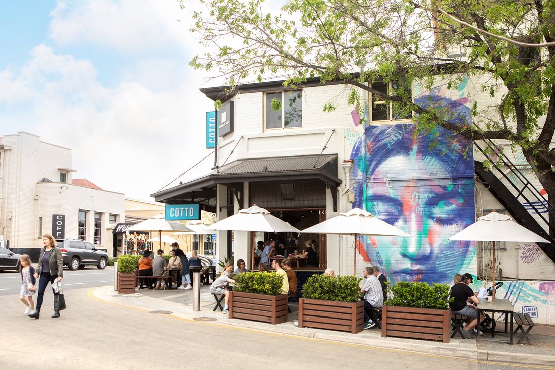 The Cotto shopfront on Prospect Road, with white umbrellas over the footpath tables and a painted mural on the wall alongside.