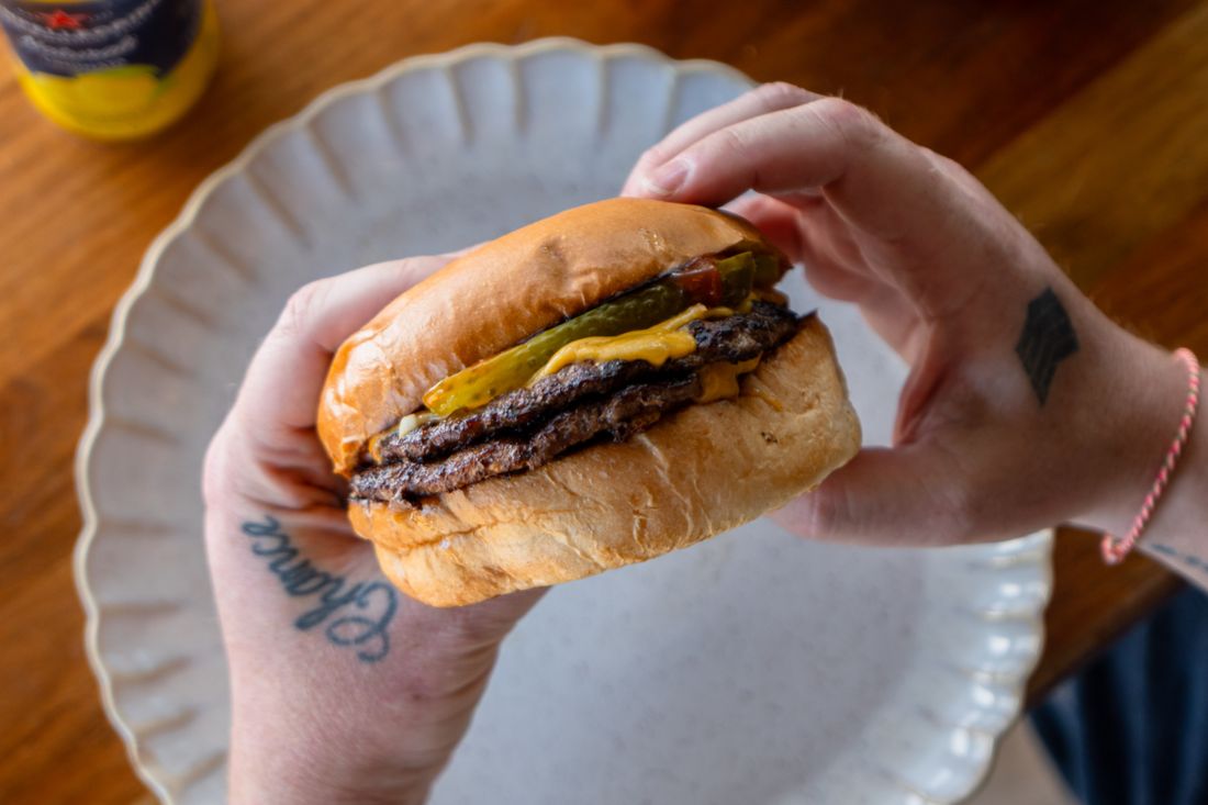 A double smash beef burger held in two hands, cheese melting over the patties.