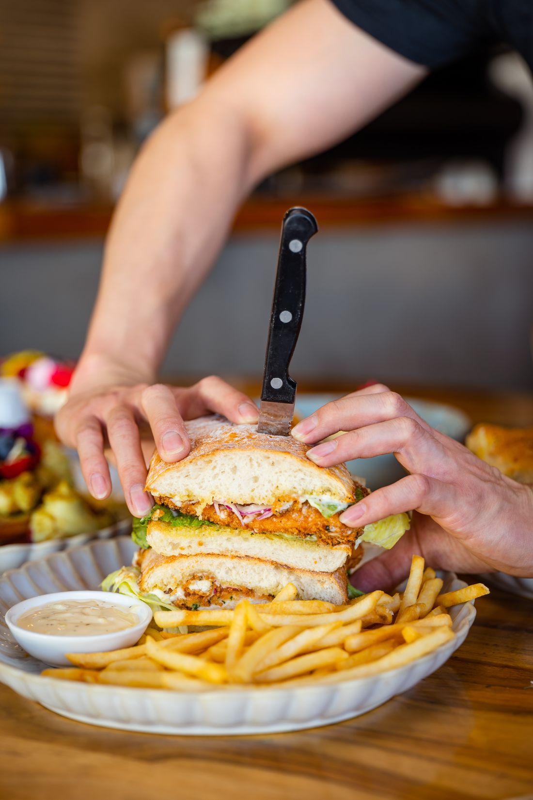 A chicken cotoletta panino being cut open, salad and fries alongside.