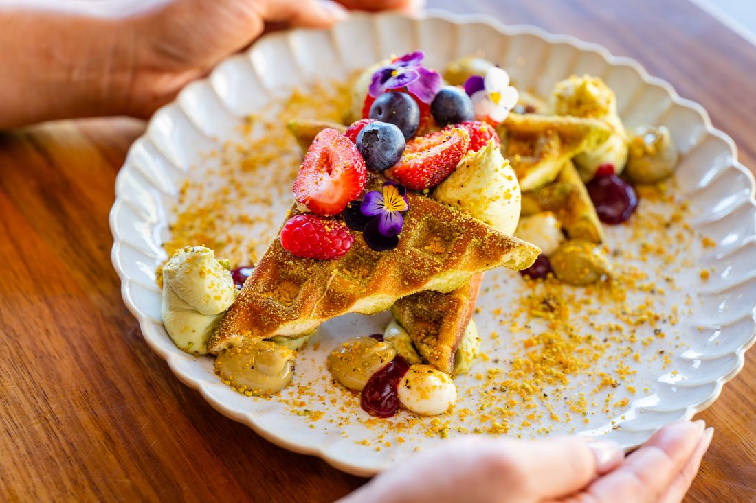 Waffles topped with berries, cream and crushed pistachio praline.